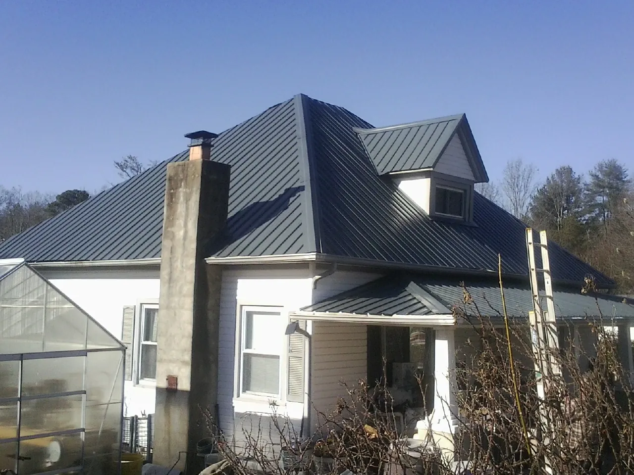 Dark blue standing seam metal roof on a white farmhouse with dormer — Slate & Tile Roof Repair by Roofing Brothers in Watford City
