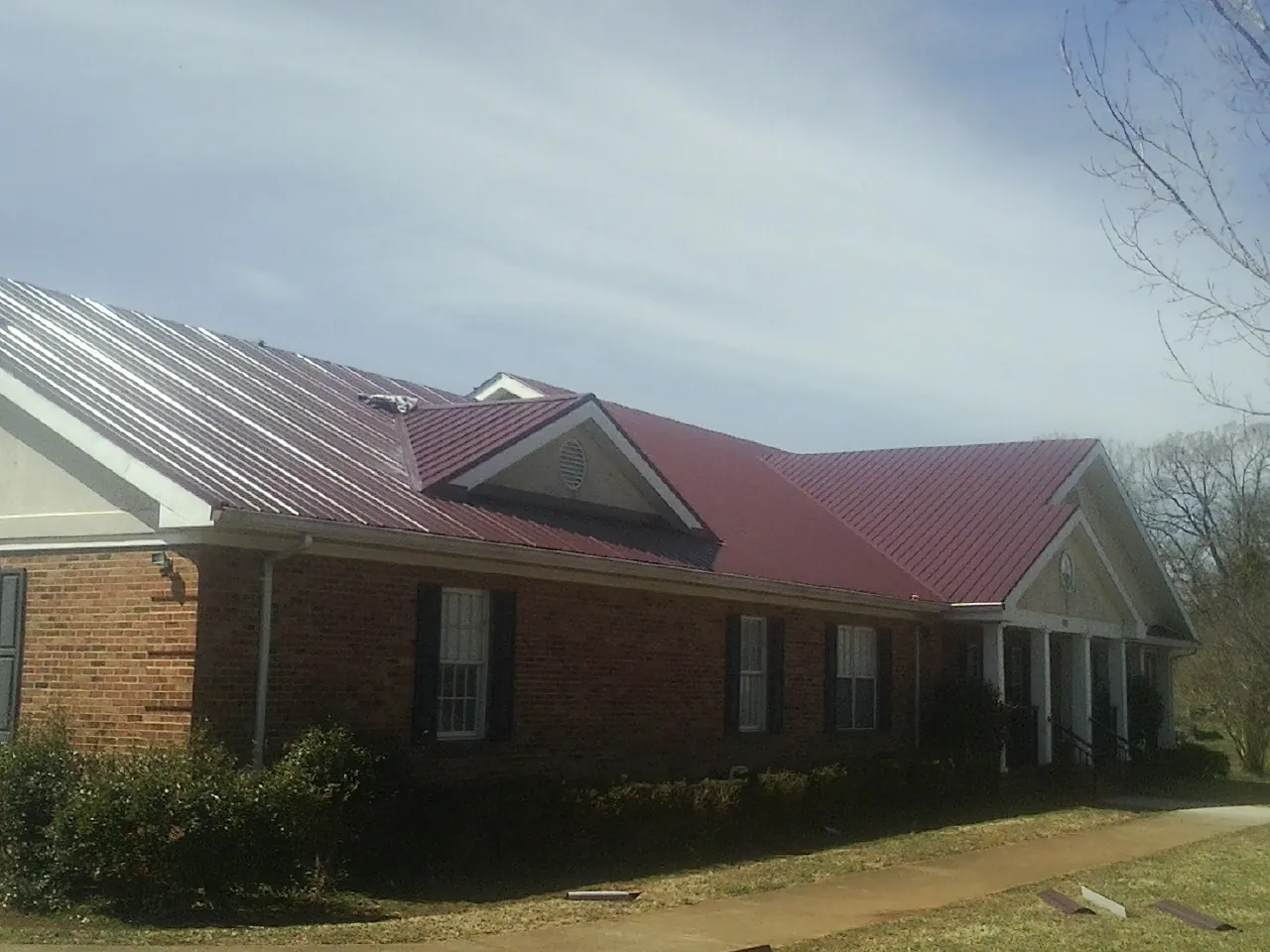 Red metal roof with gabled entries on a long brick building, from a Hail Damage Roof Repair job in Watford City