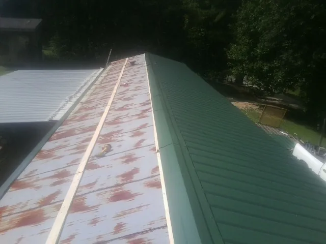 Old rusted panels beside newly installed green metal roofing — Wind Damage Roof Repair by Roofing Brothers in Watford City
