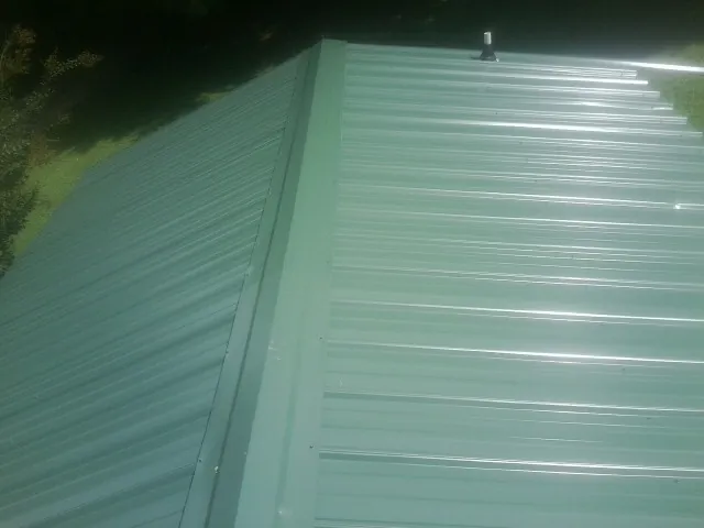 New green metal panels meeting at the ridge of a roof — Flat Roof Repair work by our crew in Watford City