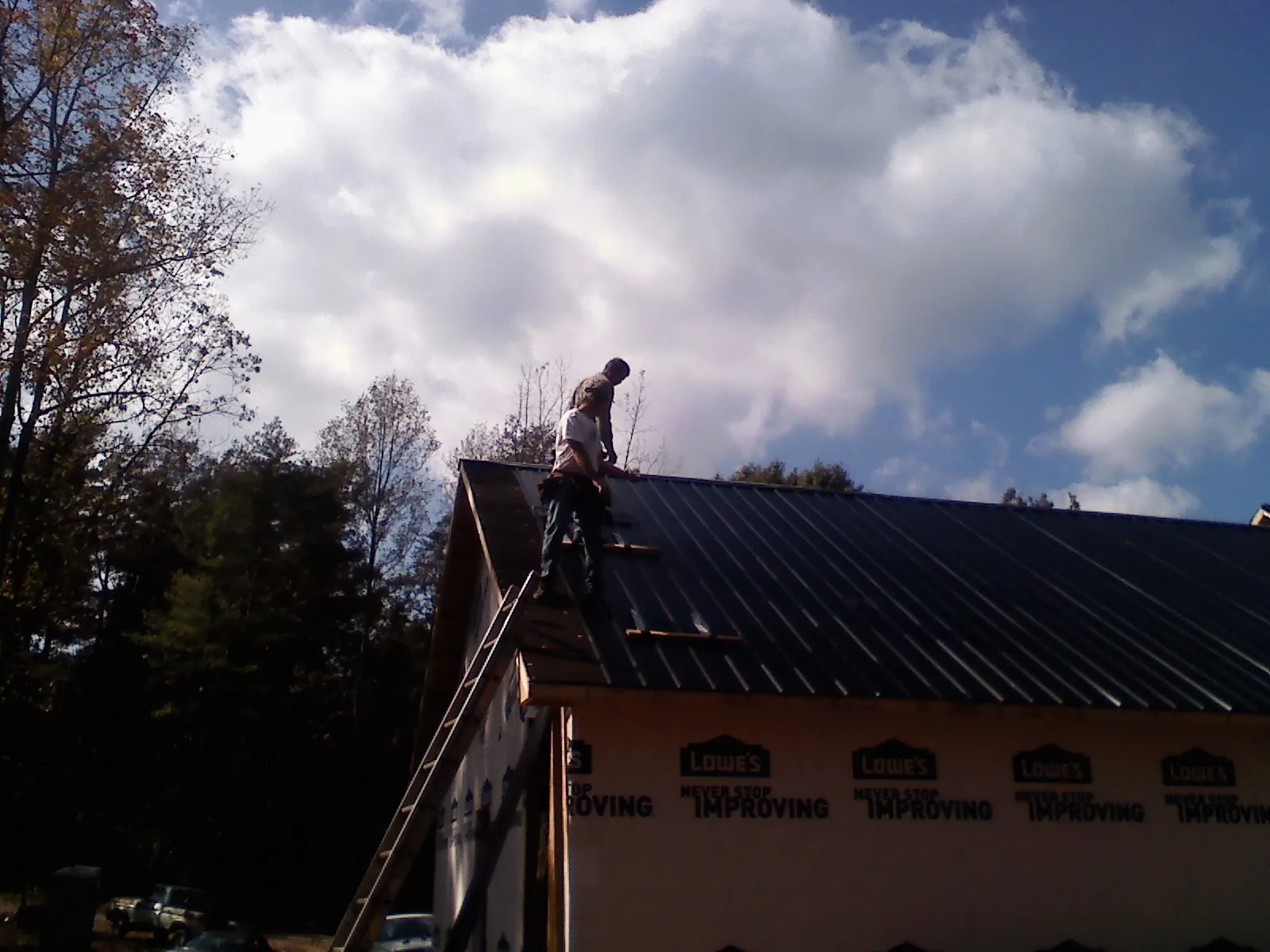 Roofer fastening dark metal panels high against a cloudy sky in Watford City
