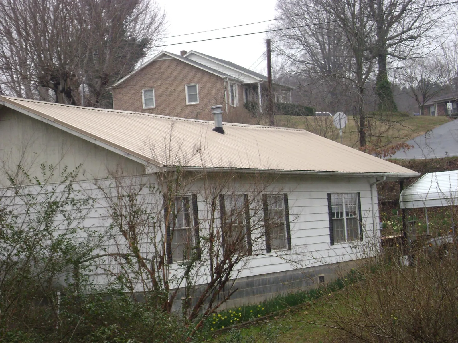 Tan metal roof on a white sided house set into a hillside — Commercial Roofing by Roofing Brothers in Watford City