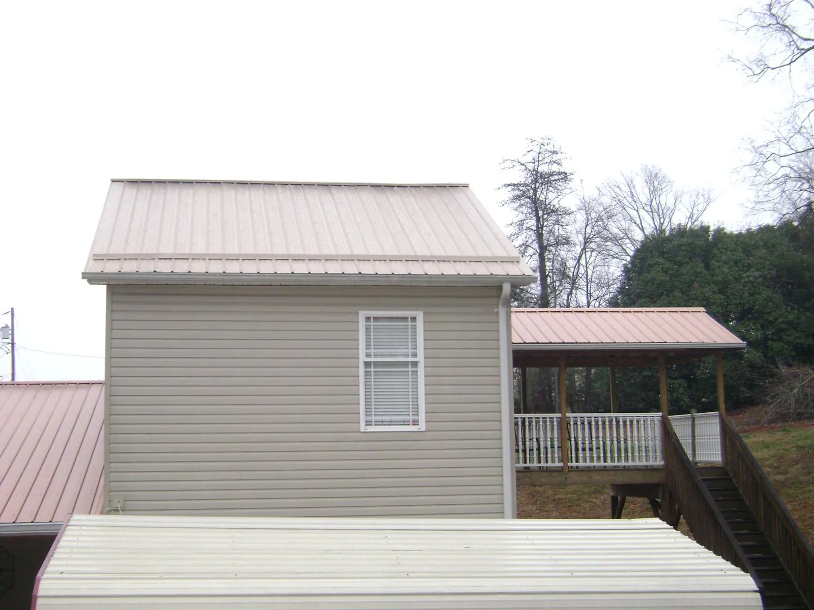 Tan metal roofs on a two story addition and attached porch, from a Roof Replacement job in Watford City